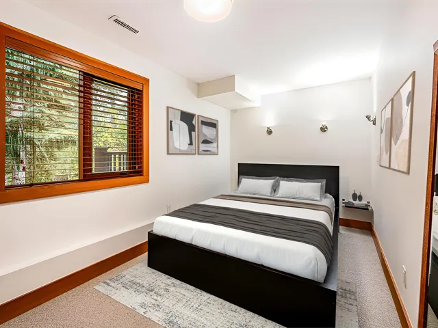 Bedroom featuring a large wood-framed window with blinds, recessed lighting, wall-mounted sconces, white walls, and light-toned carpet flooring with wood-finish baseboards