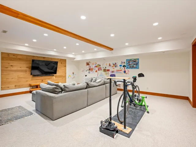 Recessed lighting illuminates this versatile lower-level space featuring light-toned carpeting and a wood-paneled accent wall