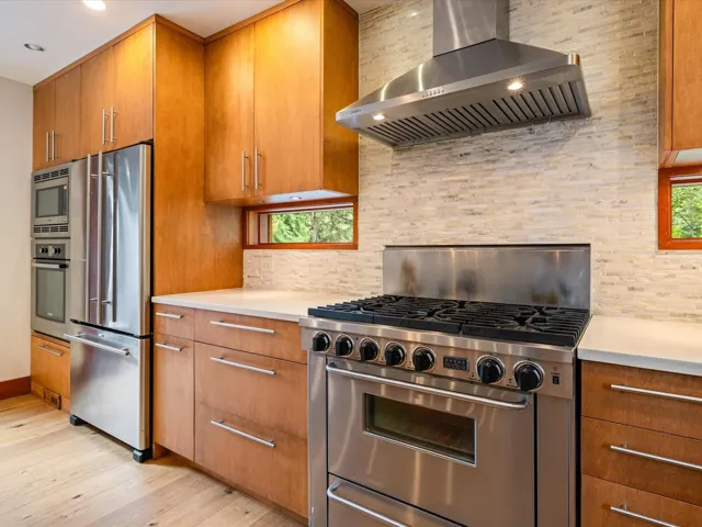 Gourmet kitchen featuring a professional-grade stainless steel gas range with a coordinating range hood, full-height stacked cabinetry, a built-in oven and microwave, and light-toned countertops