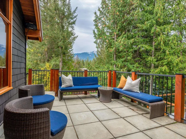 Spacious outdoor deck featuring large format tile flooring, black metal railings with natural wood posts, and a shingle-sided exterior with wood trim