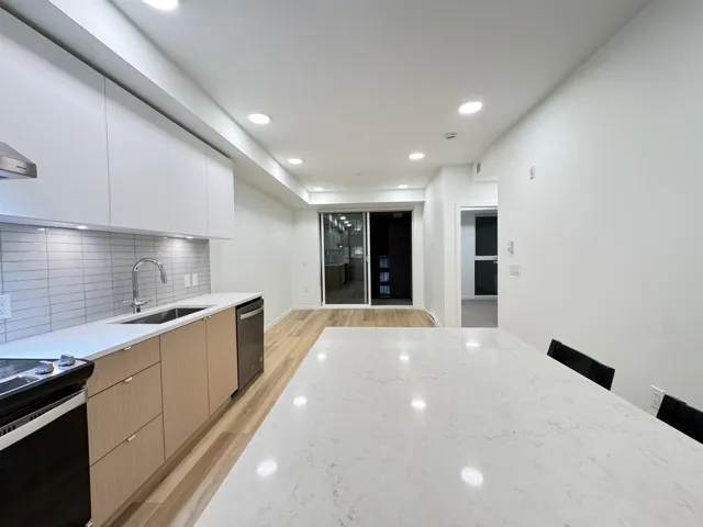 Kitchen with modern cabinets, backsplash, white cabinetry, light wood finished floors, and light stone counters