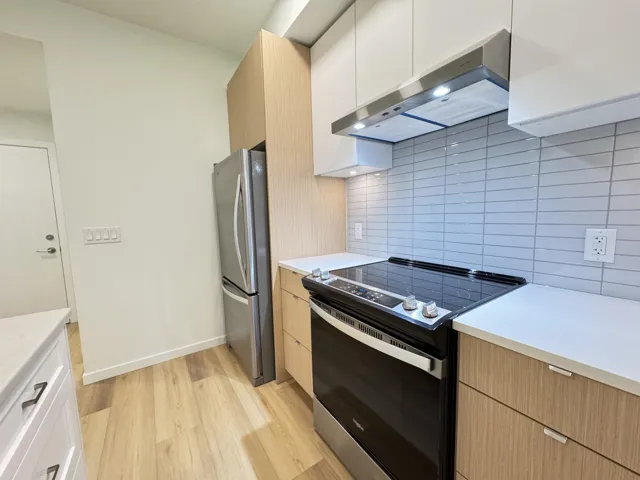 Kitchen with range with electric stovetop, under cabinet range hood, modern cabinets, light wood-style flooring, and freestanding refrigerator
