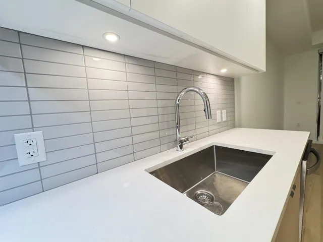 Kitchen view of light stone counters, dishwasher, white cabinets, recessed lighting, and decorative backsplash