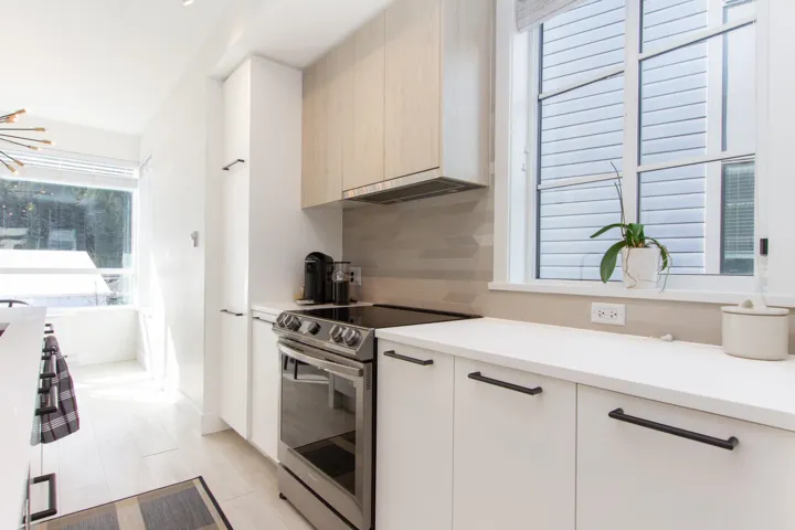 Kitchen featuring modern cabinets, under cabinet range hood, tasteful backsplash, stainless steel electric stove, and light countertops