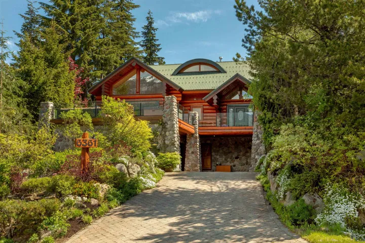 Log cabin featuring stone siding, log exterior, decorative driveway, and a balcony