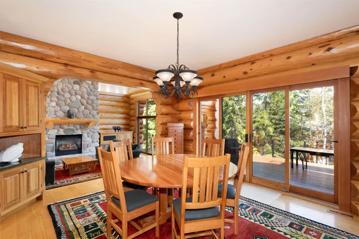 Dining space with rustic walls, a stone fireplace, a chandelier, and light wood-style flooring