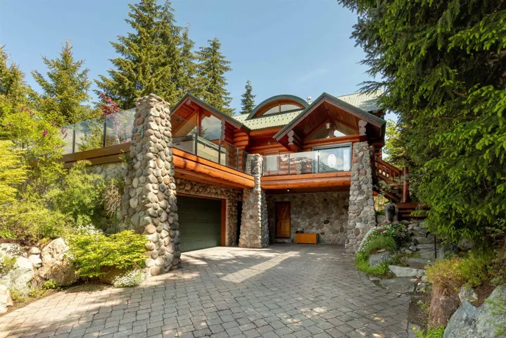 Cabin with stone siding, a balcony, decorative driveway, and a garage