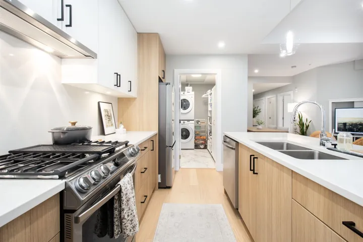 Kitchen with under cabinet range hood, stainless steel appliances, light countertops, stacked washing maching and dryer, and a sink