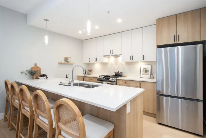 Kitchen featuring stainless steel appliances, light countertops, hanging light fixtures, a sink, and a kitchen bar