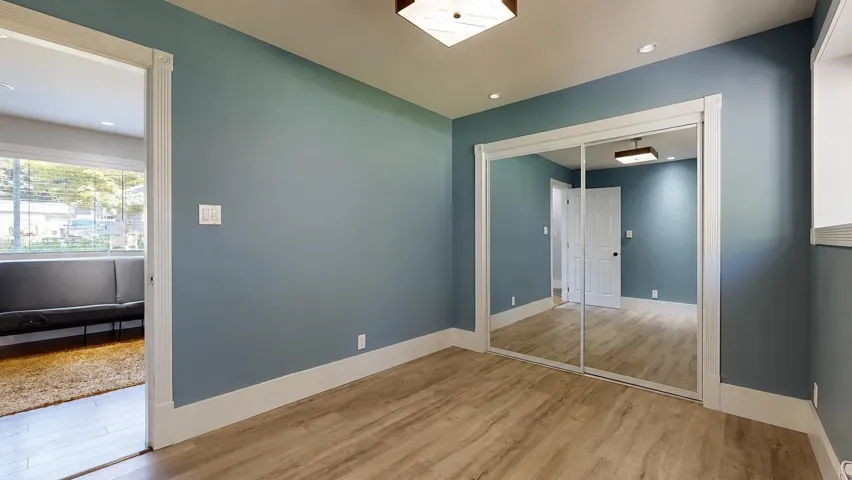 Spacious room featuring wood-finish flooring, a full-wall mirrored closet, recessed lighting, and a contemporary ceiling fixture