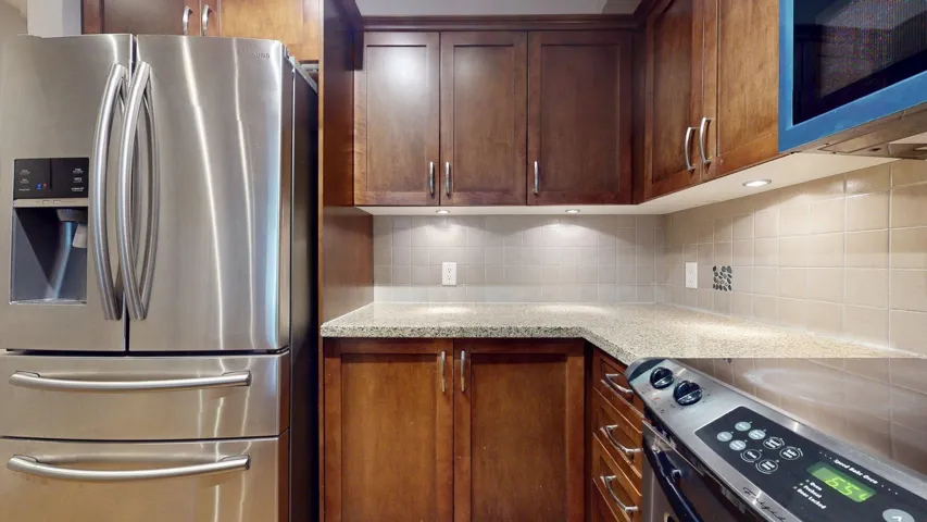 Kitchen featuring appliances with stainless steel finishes, light stone countertops, and backsplash