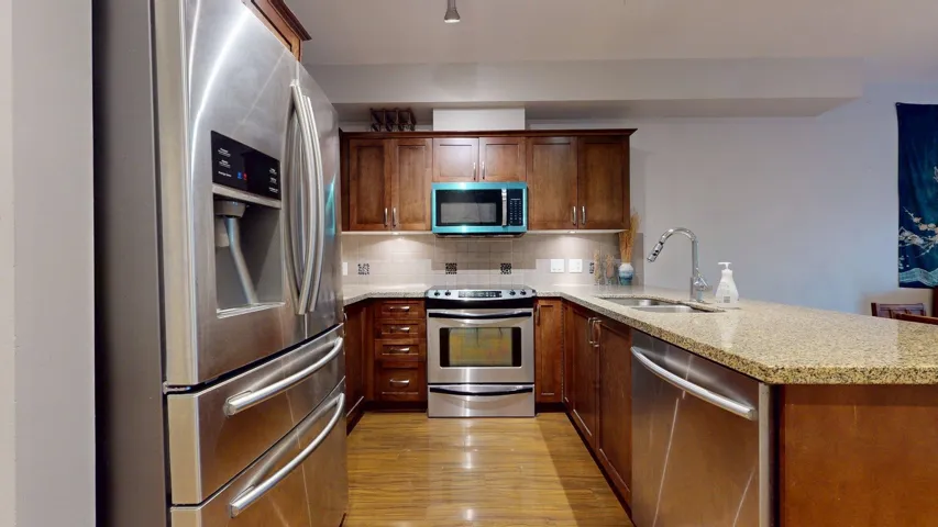 Kitchen with appliances with stainless steel finishes, decorative backsplash, a peninsula, light stone counters, and light wood-style floors