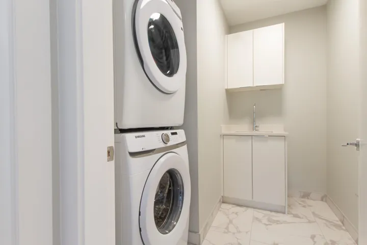 Clothes washing area featuring baseboards, marble finish floor, a sink, stacked washer and dryer, and cabinet space