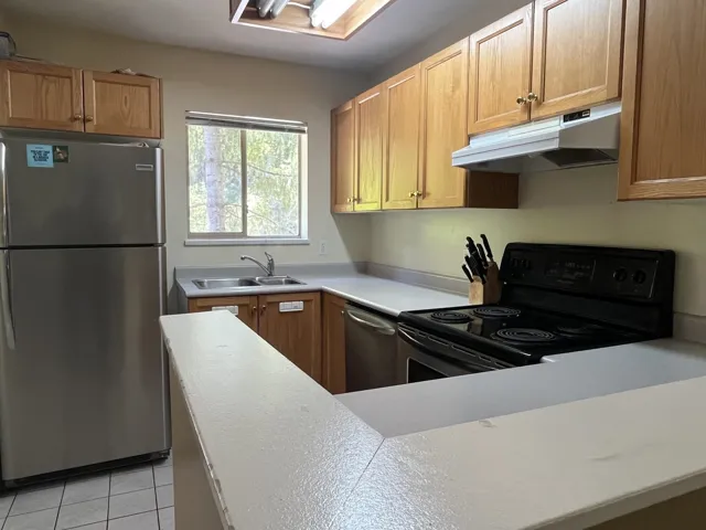 Kitchen featuring wood cabinetry, stainless steel refrigerator, black electric range, double basin sink, and a skylight