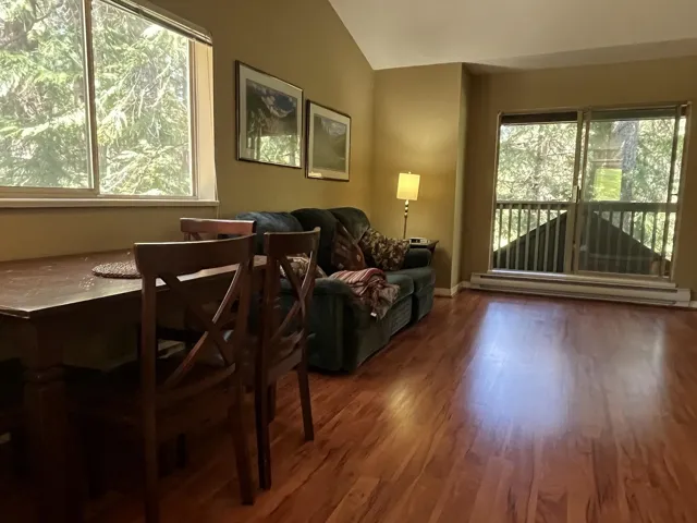 Inviting living area featuring warm wood-finish flooring, a vaulted ceiling, and ample natural light through large windows