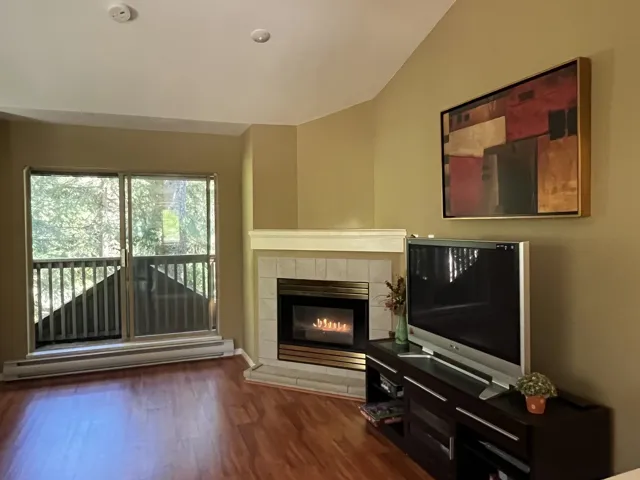 Living area with wood-finish flooring, a corner fireplace featuring a tile surround and hearth, and a sliding glass door opening to an outdoor space