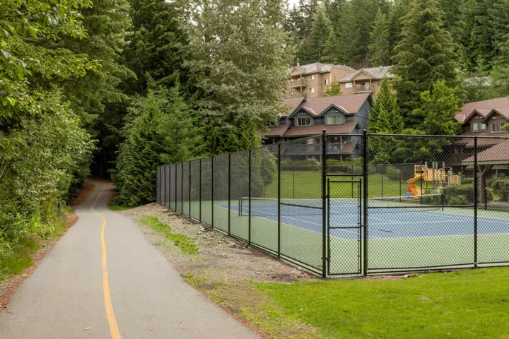 Outdoor tennis court with chain-link fencing, situated alongside a paved pathway