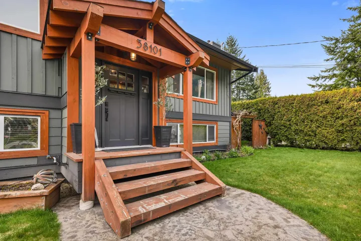 Exterior featuring a dark gray facade with natural wood accents, a covered entry porch, a dark gray paneled front door with upper glass inserts, and a stamped concrete pathway