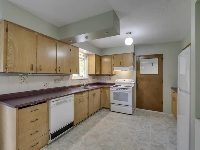 Kitchen featuring white appliances, dark countertops, decorative backsplash, under cabinet range hood, and a textured ceiling