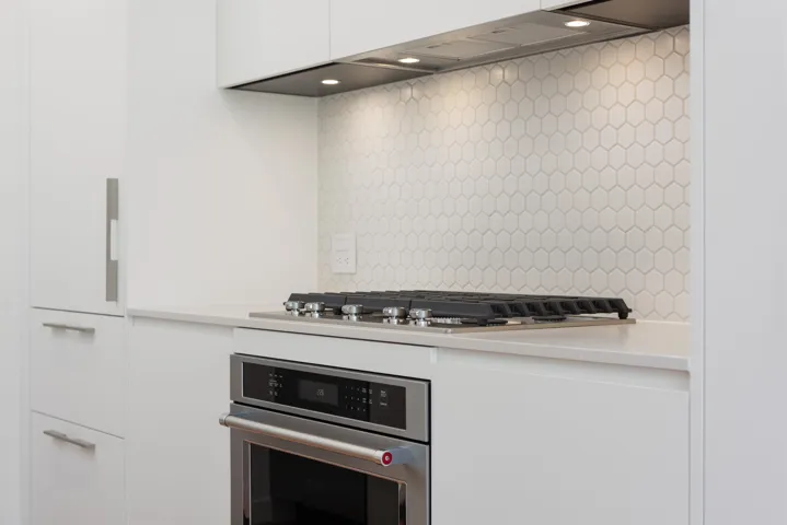 Kitchen featuring stainless steel appliances, white cabinetry, light countertops, premium range hood, and tasteful backsplash