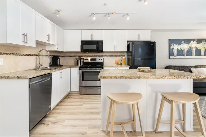 Kitchen featuring black appliances, a kitchen bar, white cabinetry, and backsplash
