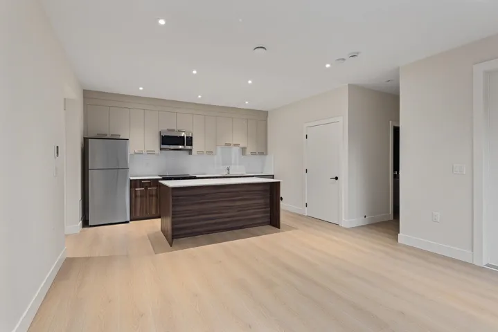 Kitchen with appliances with stainless steel finishes, light wood-type flooring, light countertops, recessed lighting, and a center island