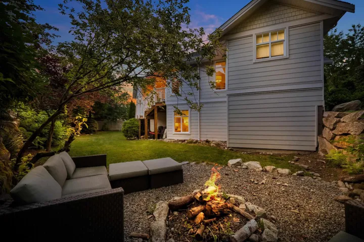 Spacious backyard featuring a fire pit area with gravel ground cover, a grassy lawn, and mature trees