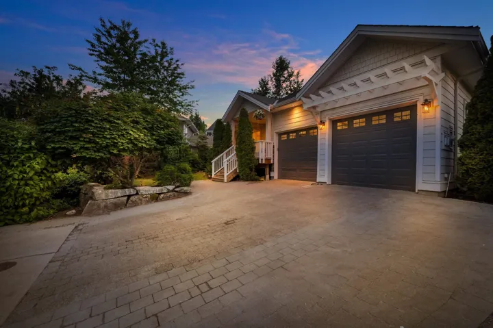 Exterior featuring light-colored siding, a two-car garage with dark paneled doors and window accents, and an overhead pergola architectural detail