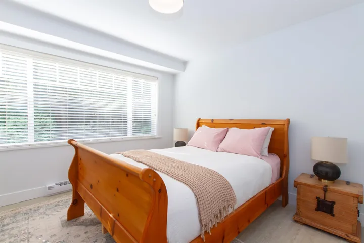 Bright room featuring a large window with horizontal blinds, light-toned walls, and wood-finish flooring