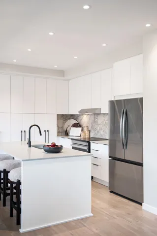 Modern kitchen featuring an expansive island with a matte black faucet, stainless steel appliances, a stone backsplash, extensive white cabinetry, and wood-finish flooring