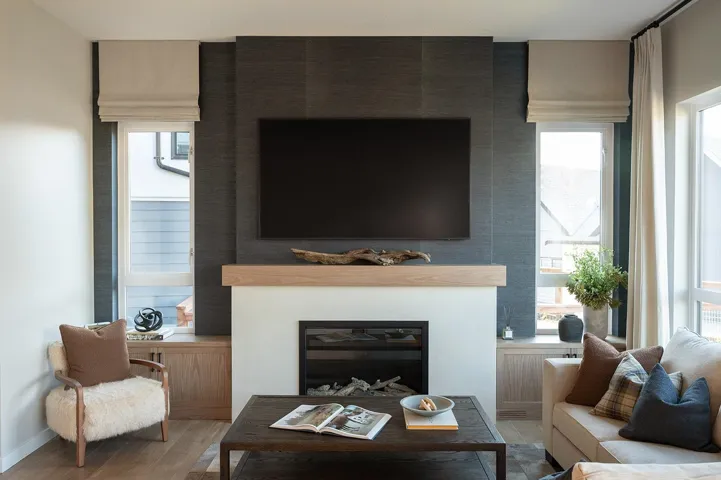 Living area featuring a modern fireplace with a light wood mantel, a dark textured accent wall, and built-in cabinetry flanking the fireplace