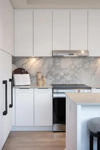 Modern kitchen featuring white flat-panel cabinetry, a stainless steel range hood, and a marble-patterned backsplash