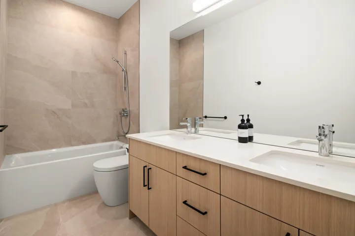 Bathroom with toilet, a sink, double vanity, and bathtub / shower combination