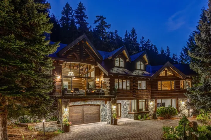 Cabin with stone siding, decorative driveway, an attached garage, and log siding