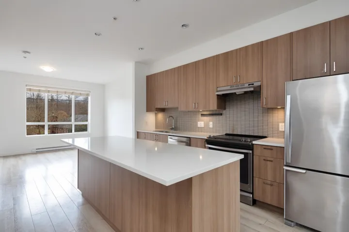 Kitchen with tasteful backsplash, under cabinet range hood, light countertops, stainless steel appliances, and a baseboard radiator