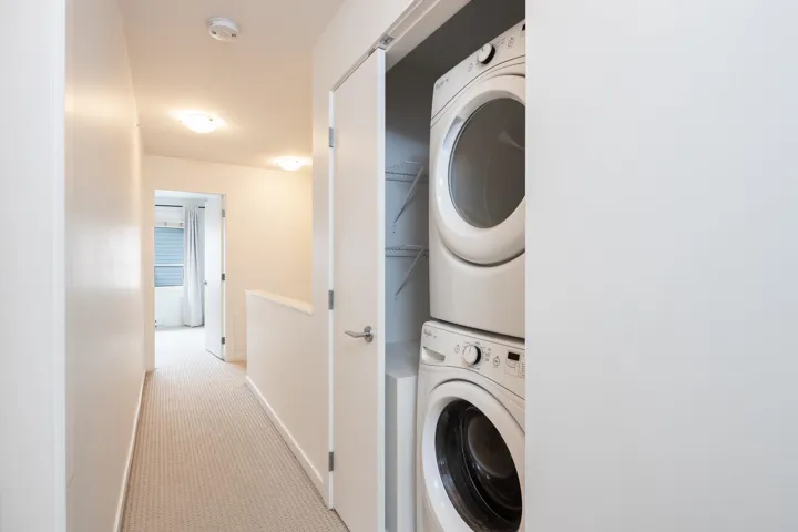 Clothes washing area featuring laundry area, stacked washer and clothes dryer, baseboards, and carpet floors