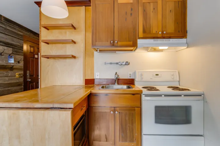 Kitchen with white electric range oven, under cabinet range hood, a sink, open shelves, and brown cabinetry