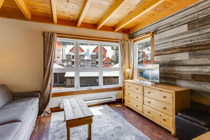 Living area with beamed ceiling, wood walls, wood ceiling, and dark wood-style flooring