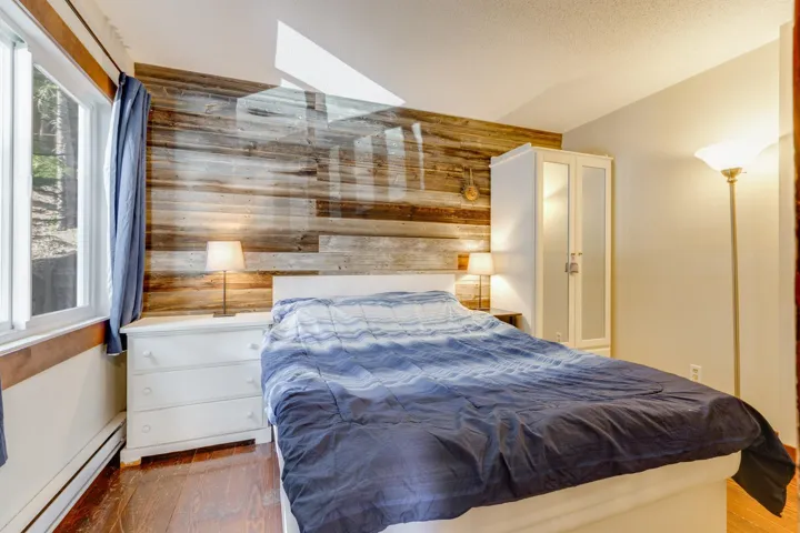 Bedroom with a baseboard radiator, vaulted ceiling, wooden walls, and wood finished floors