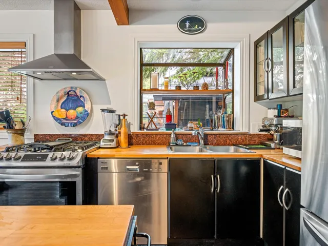Kitchen with wall chimney range hood, appliances with stainless steel finishes, wooden counters, and glass insert cabinets