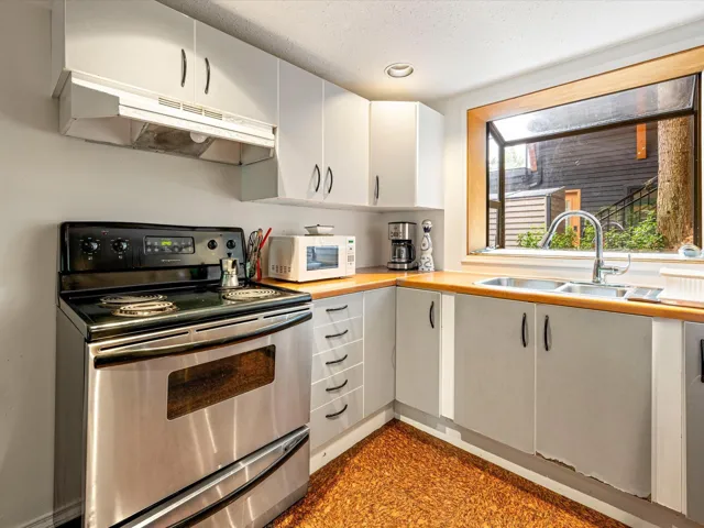 Kitchen featuring stainless steel electric stove, white microwave, under cabinet range hood, white cabinets, and butcher block countertops
