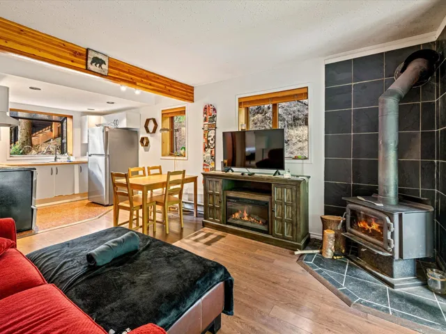 Living area with a wood stove, light wood-style floors, beam ceiling, and a textured ceiling