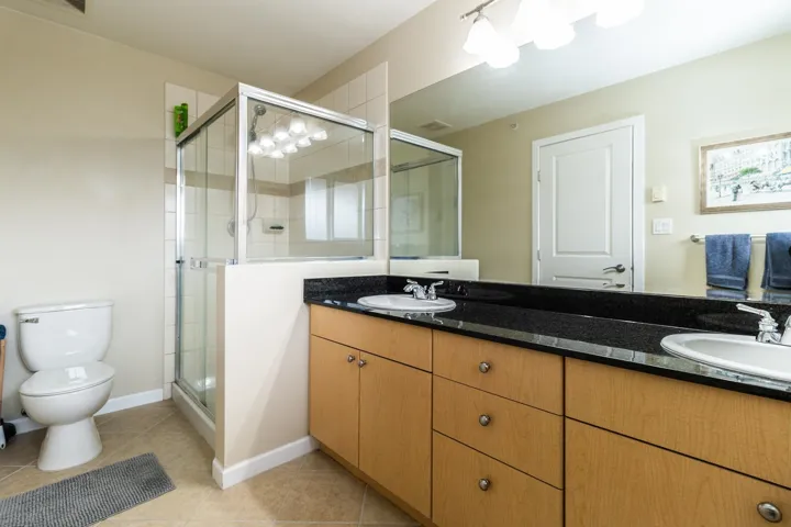 Full bath featuring double vanity, a shower stall, and light tile patterned flooring