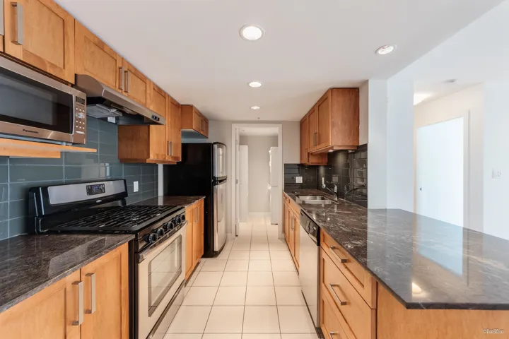 Kitchen with stainless steel appliances, under cabinet range hood, a sink, light tile patterned flooring, and backsplash