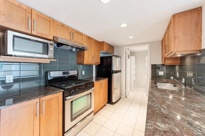 Kitchen with appliances with stainless steel finishes, under cabinet range hood, a sink, backsplash, and light tile patterned floors