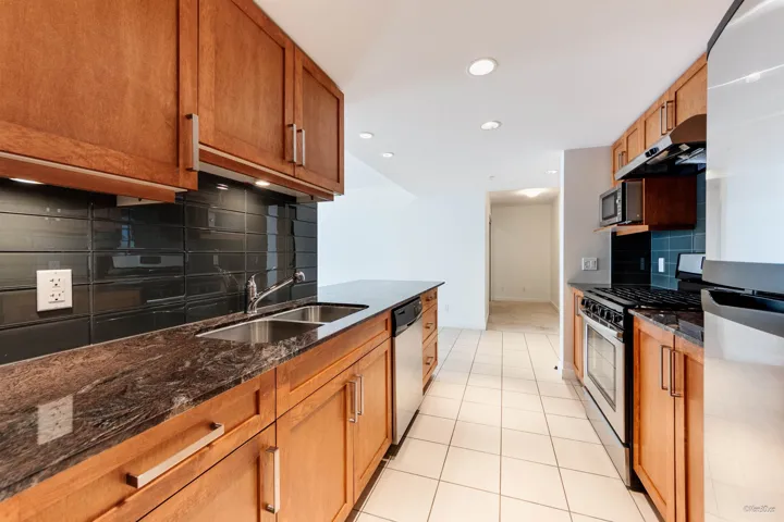 Kitchen with appliances with stainless steel finishes, a sink, tasteful backsplash, extractor fan, and dark stone countertops