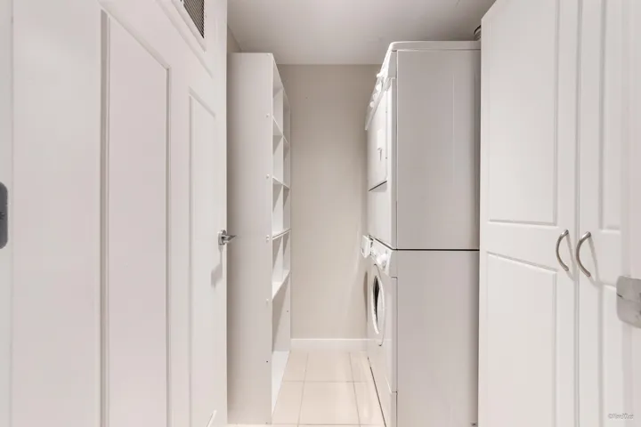 Washroom with estacked washer and dryer, light tile patterned floors, and baseboards
