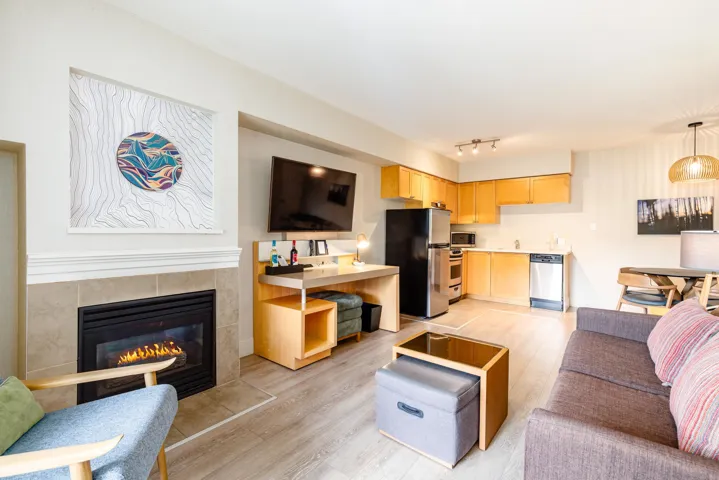 Open-concept living space featuring a gas fireplace with a tiled surround, wood-finish flooring, a full kitchen with stainless steel appliances, and track lighting