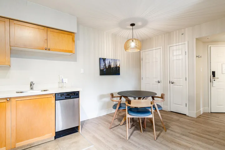 Kitchenette featuring light wood cabinetry, a stainless steel dishwasher, and a white countertop with an undermount sink