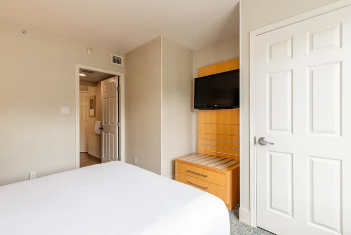 Neutral-toned bedroom featuring a built-in entertainment unit with a mounted television and wood-finish cabinetry
